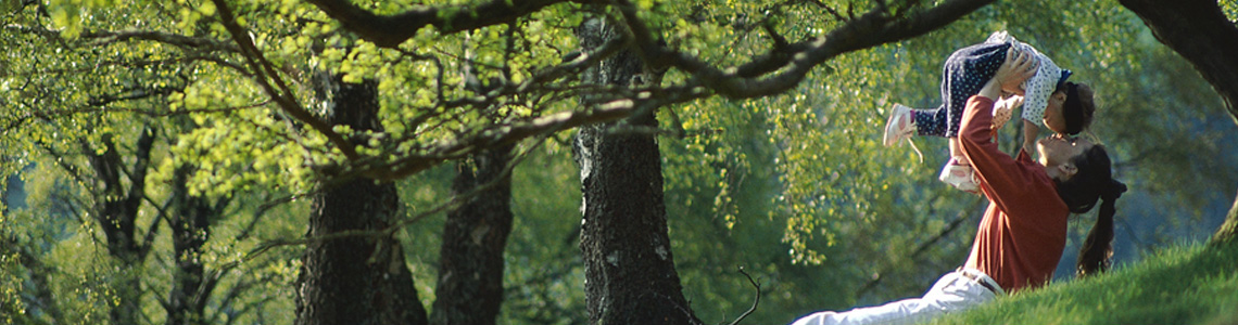 Mom holding child under tree.